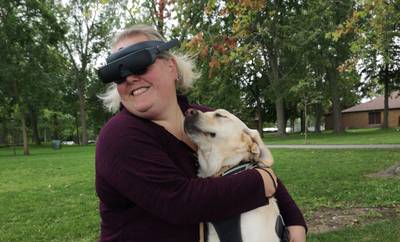 Jaclyn Pope of Oshawa, Ontario, received eSight eyewear through a scholarship program in 2021. Pope is a blonde woman and is smiling while holding a large light-colored dog.