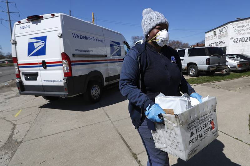 In this April 2, 2020, file photo, a United States Postal  Service worker makes a delivery with gloves and a mask in Warren, Mich.