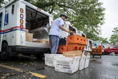 Letter carriers load mail trucks for deliveries at a U.S. Postal Service facility in McLean, Va., Friday, July 31, 2020.