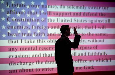 The Oath of Office is projected on a screen behind an ROTC cadet as he takes the Oath at Clemson University, May 11, 2022.