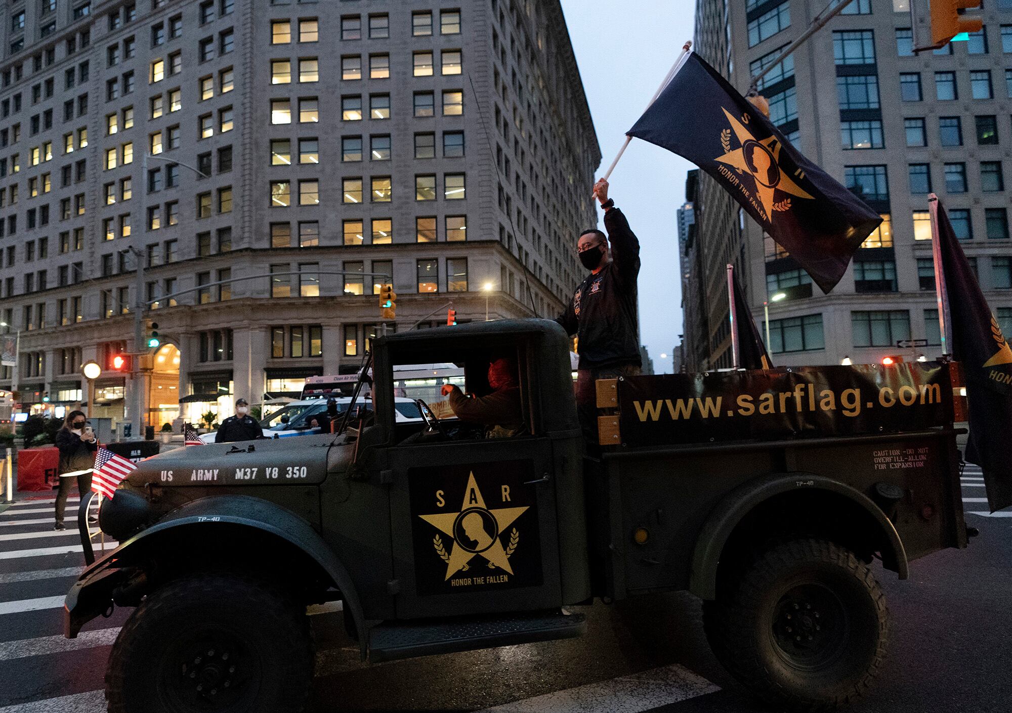 A man waves a flag as he stands in the back of a military vehicle during a Veterans Day parade, Wednesday, Nov. 11, 2020, in New York.