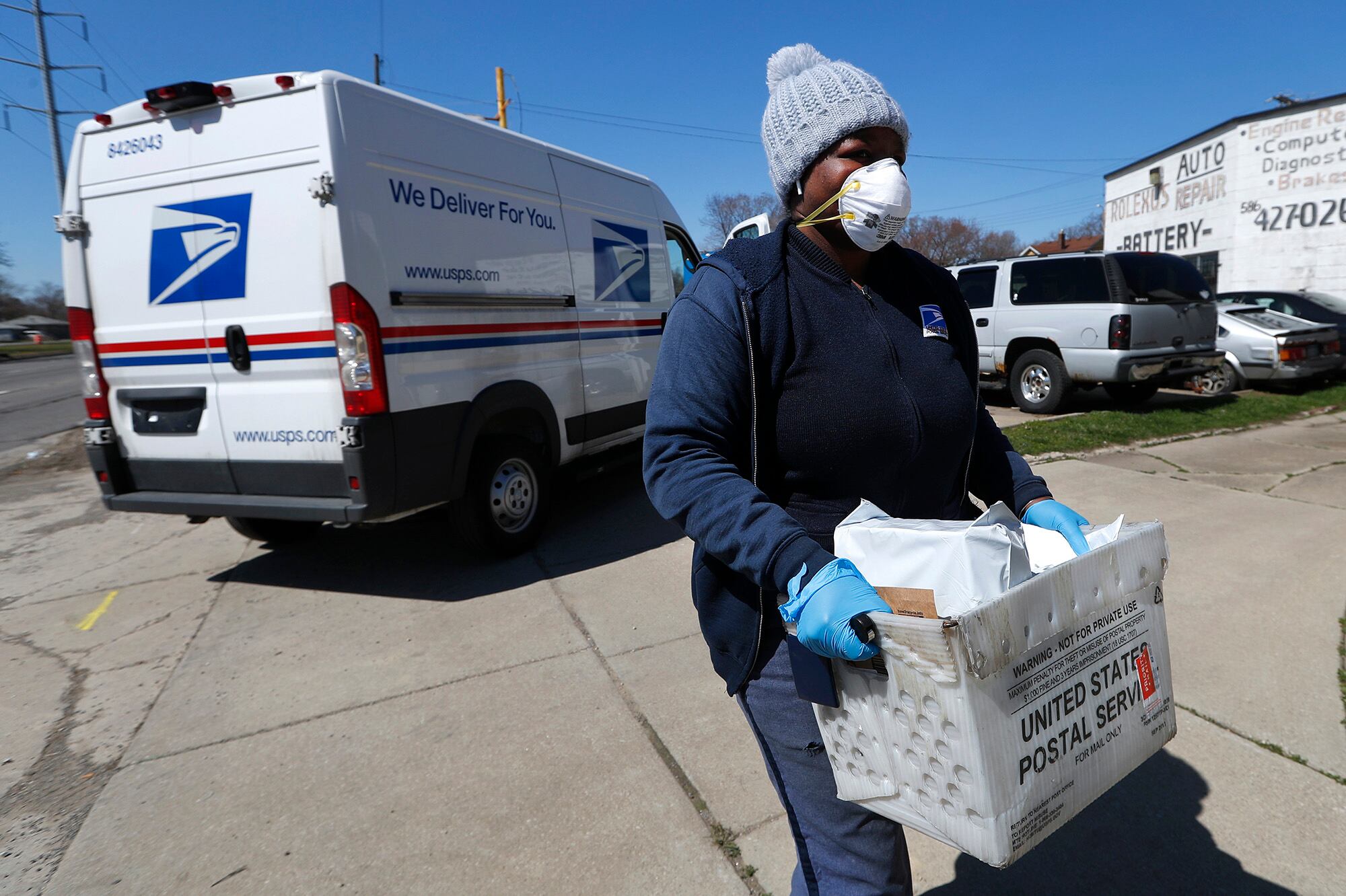 In this April 2, 2020, file photo, a United States Postal Service worker makes a delivery with gloves and a mask in Warren, Mich.